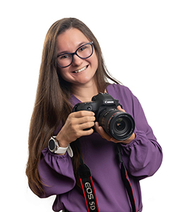 headshot of woman wearing glasses and purple shirt holding camera